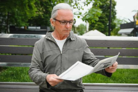 Portrait of senior man reading on bench during summer day.